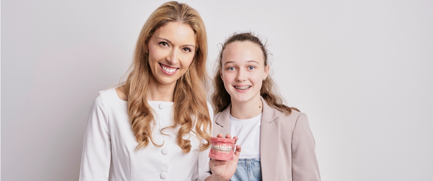 Orthontist with happy patient showing brackets. Kieferorthopädin mit glücklicher Teenager Patientin, die beim Lachen ihre feste Zahnspange mit Metallbrackets zeigt.